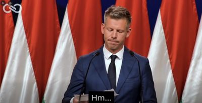 Péter Magyar at a lectern in front of Hungarian flags, looking down at a sheet of paper.