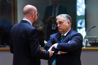 Viktor Orbán, arms crossed, listening to Charles Michel, who stands with his back to the camera.