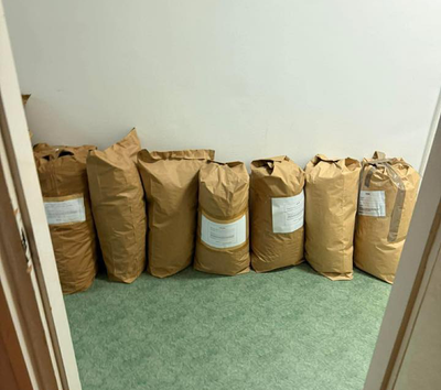 Seven large, sealed brown paper sacks lined up against the wall of an office room.